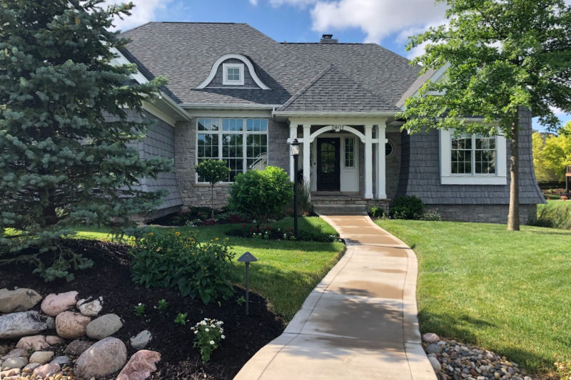 House with gray roof and beutiful landscape in front of it